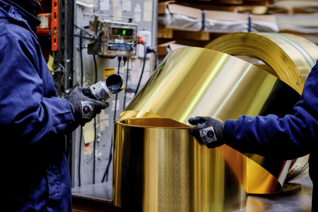 Operarios manipulando bobina de lámina de latón en planta industrial para aplicaciones eléctricas y fabricación metalúrgica
