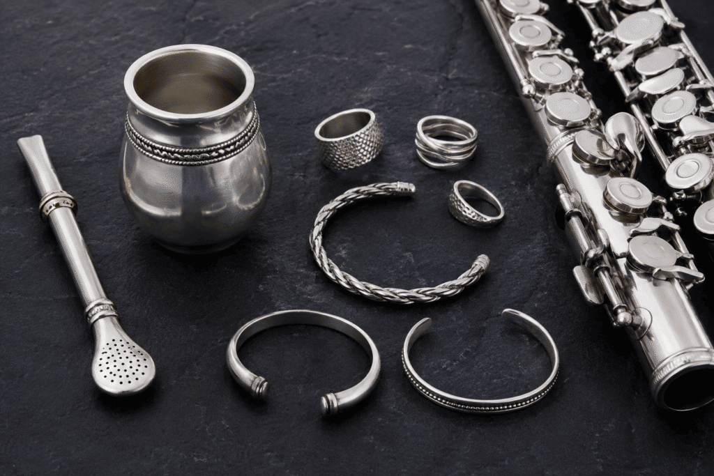 Productos fabricados en alpaca metálica: bombilla de mate, joyería artesanal y piezas para instrumentos musicales sobre fondo oscuro, fotografía de producto de alta calidad.